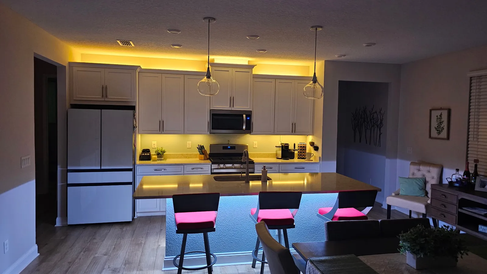 A white kitchen run warm, island glowing under magenta stools